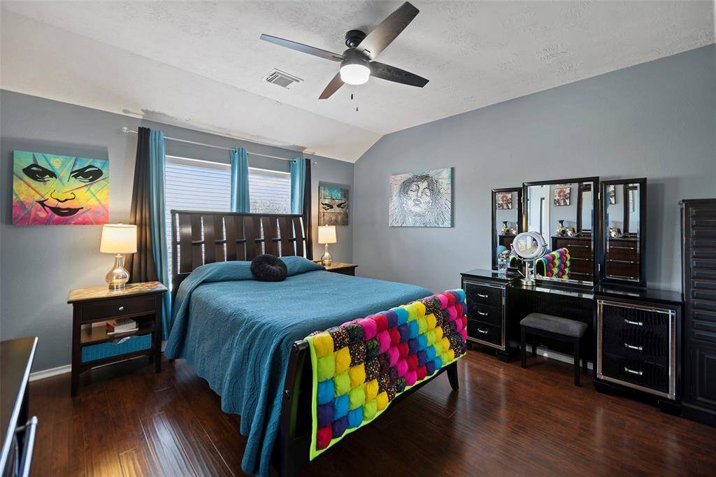 The Primary bedroom offers a cozy and modern feel with dark wood flooring and walls painted in a soft gray. The room is well-lit with natural light from the window, and has a ceiling fan for comfort.
