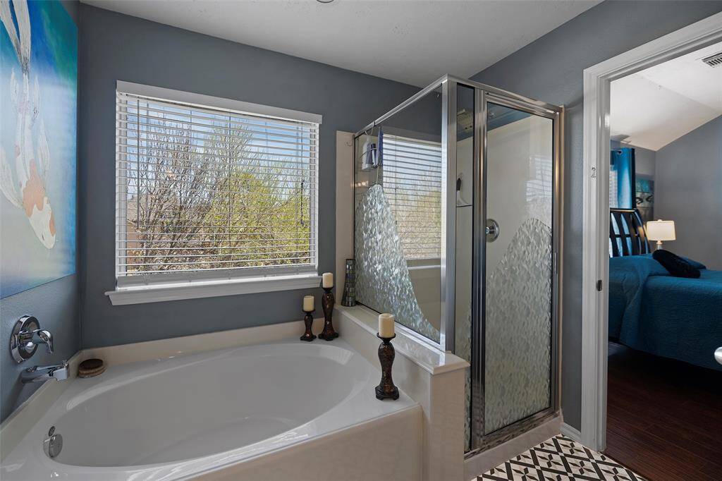 The Primary bathroom has a spacious bathtub and a separate glass shower, accented by a window with a view of greenery.