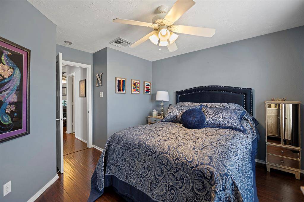 This cozy third bedroom includes a ceiling fan, hardwood floors, with sufficient light coming in.