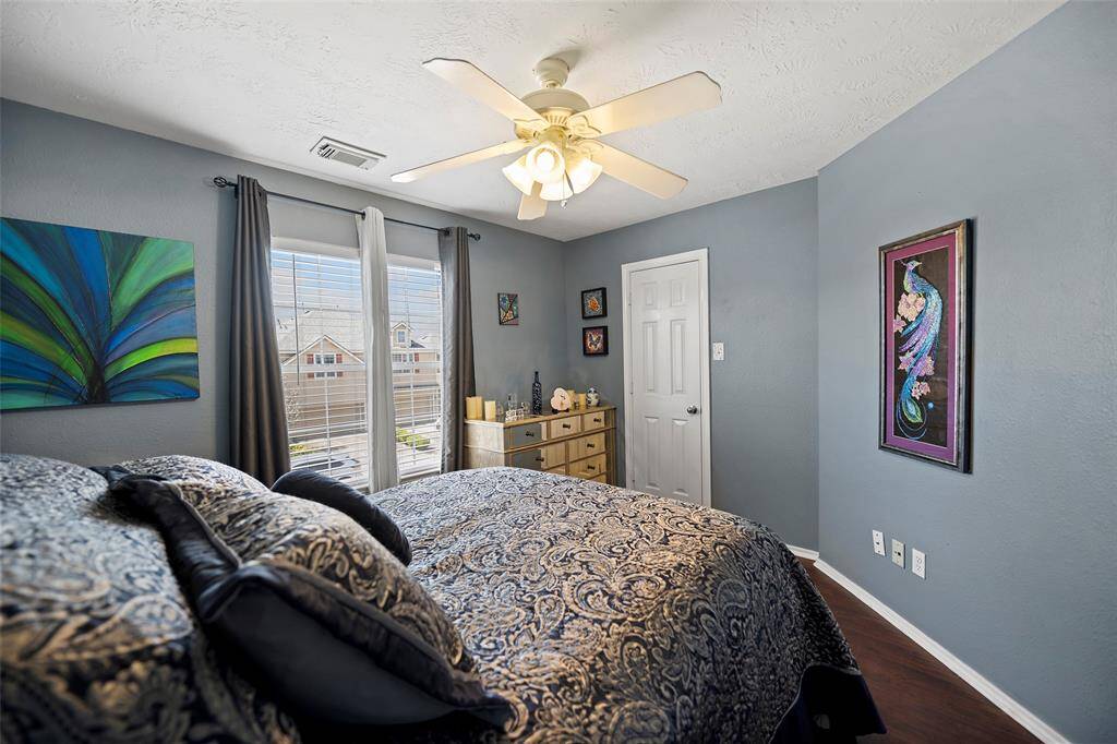 This cozy bedroom features soft blue walls, a ceiling fan, and large windows with elegant drapes, providing ample natural light.