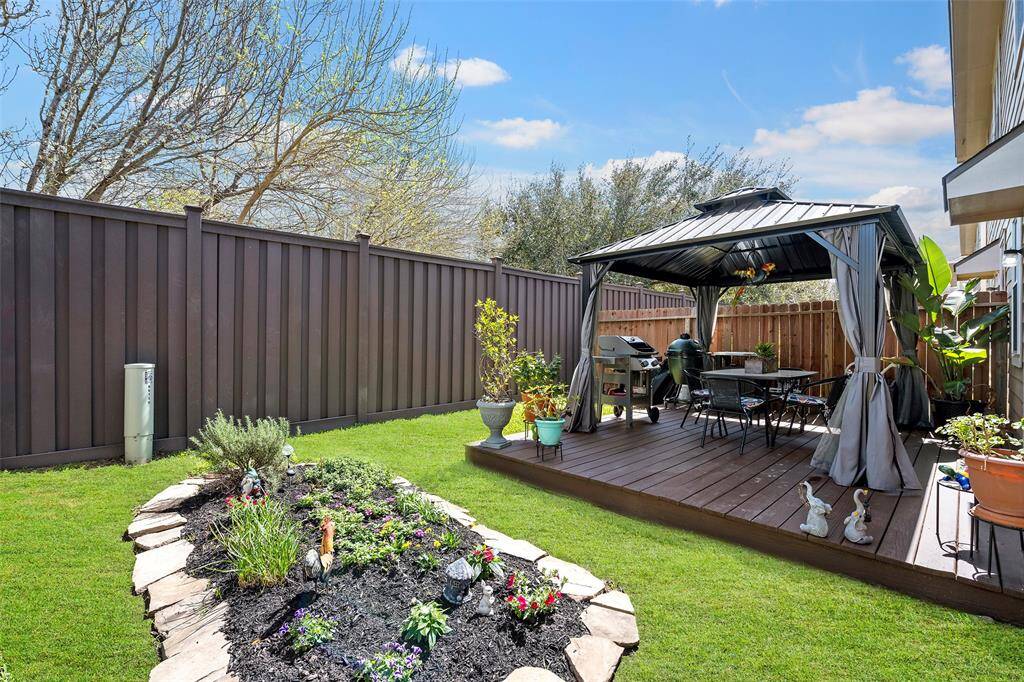 Backyard featuring a charming gazebo on a wooden deck, ideal for outdoor dining and relaxation. It includes a barbecue grill and is surrounded by a well-maintained lawn with flower bed.