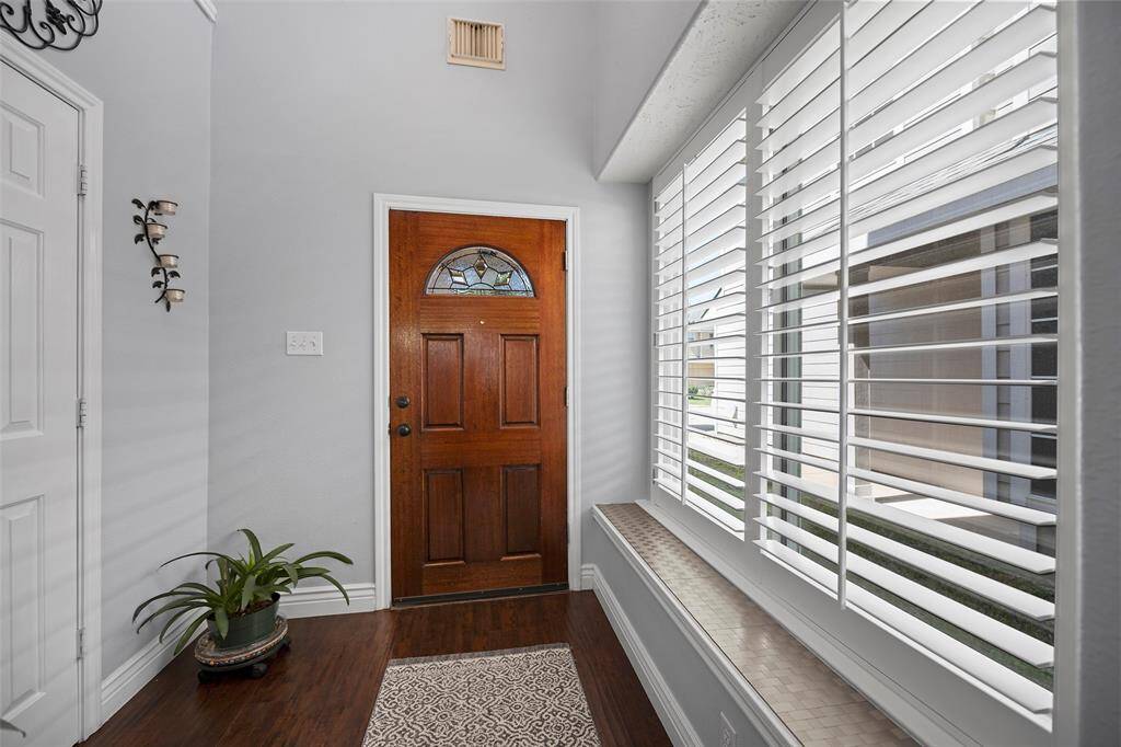 Inviting entryway with a rich wooden front door. The space features large windows with plantation shutters, letting in ample natural light.