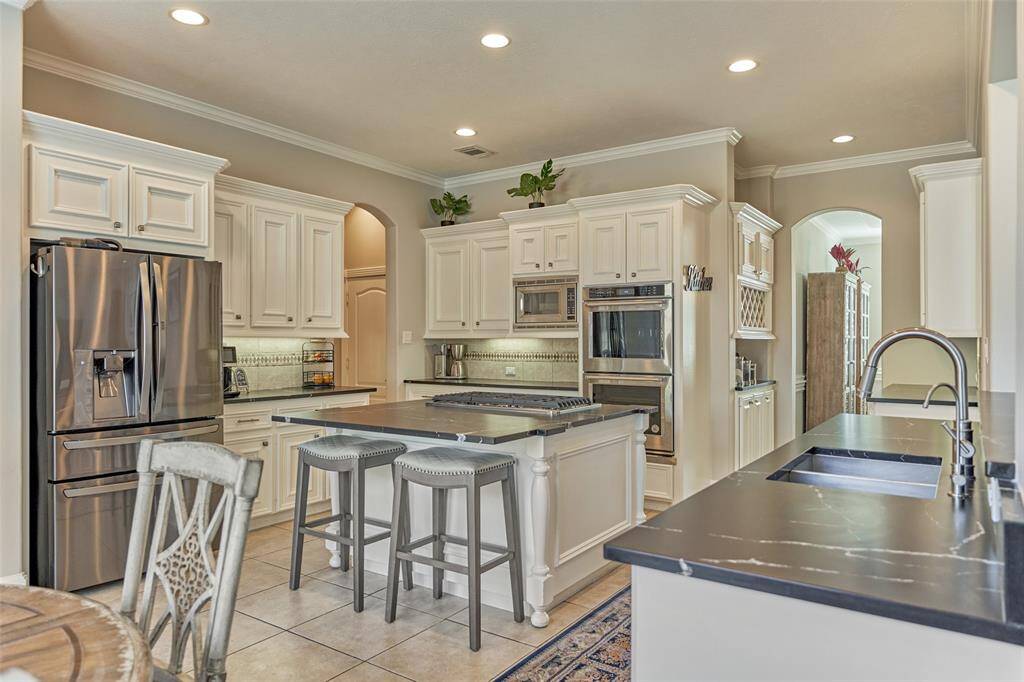 Sleek open-concept kitchen featuring updated stainless steel appliances, a functional gas stove on the island, and stunning leathered quartzite countertops.