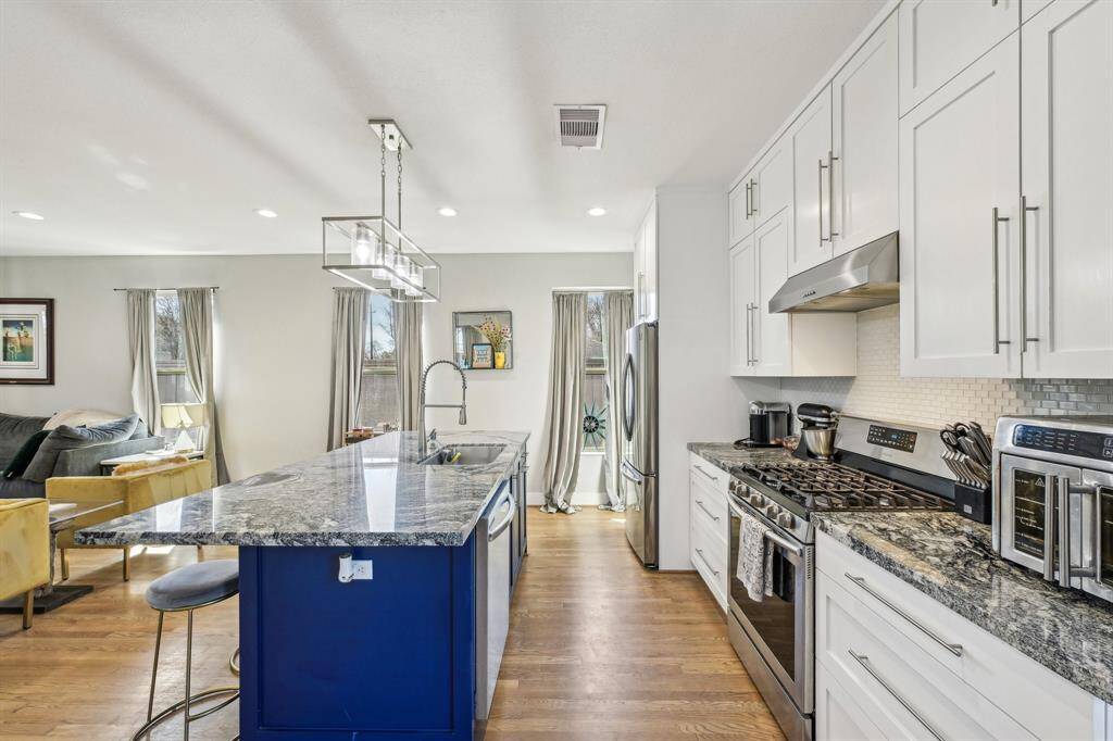 This open-concept living area features a modern kitchen with a stylish granite island, stainless steel appliances, and elegant lighting. The space flows into a cozy living room with ample natural light, hardwood floors, and a comfortable sitting area, ideal for entertaining or relaxing.