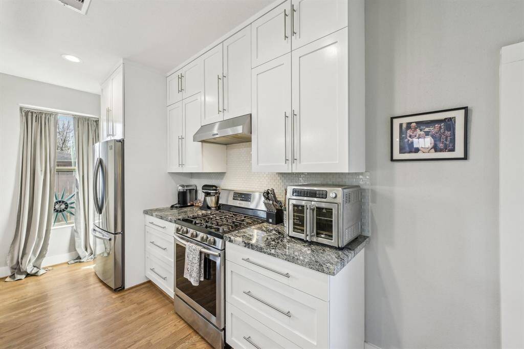 This photo showcases a modern, open-concept living space with a sleek kitchen island featuring granite countertops and a built-in sink. The room is bright, with ample natural light from large windows, and includes a cozy living area with comfortable seating. Neutral tones and contemporary lighting add to the inviting atmosphere.