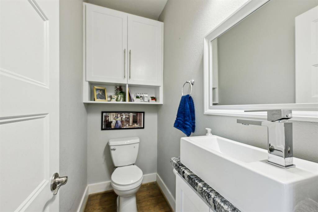 This photo shows a hallway with light wood flooring, a modern stacked washer and dryer unit, and access to a bathroom with tiled walls. The hallway leads to other rooms with a glimpse of a room featuring a bold wall color.