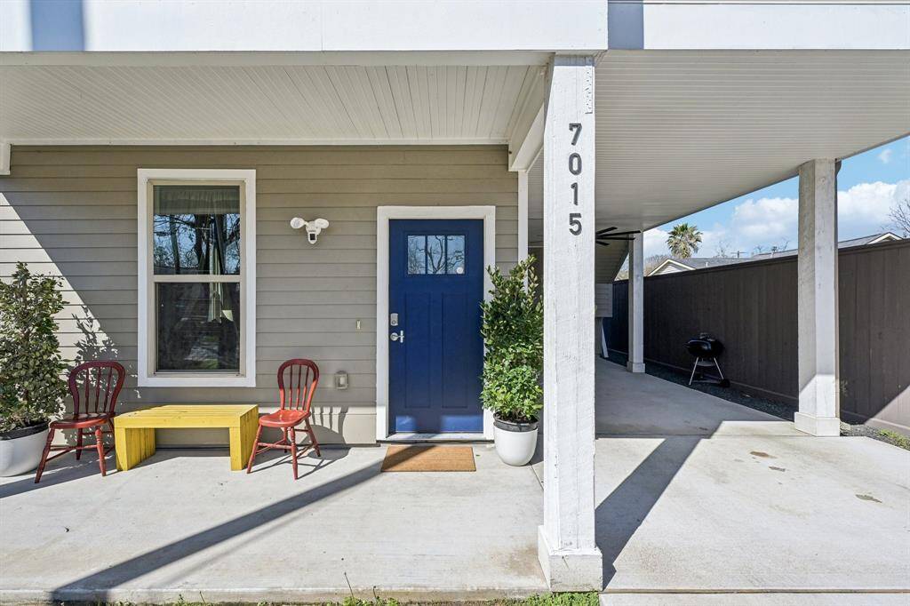 Charming home entrance with a bold blue door and a cozy porch setup. Features a covered carport, modern siding, and inviting seating area perfect for relaxing outdoors.