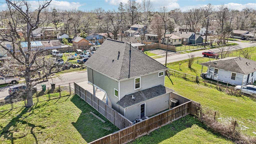 This photo showcases a two-story home with a fenced backyard, situated on a spacious lot. The surrounding neighborhood has mature trees and a mix of residential properties. The house features a sloped roof and a small patio area.