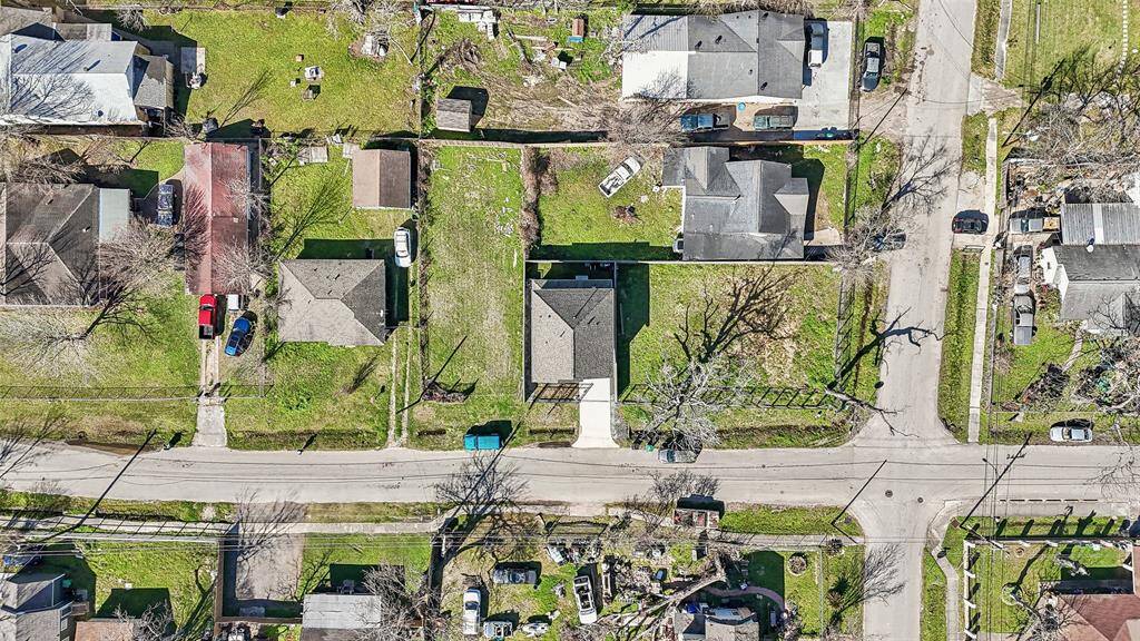 This aerial photo shows a suburban neighborhood with several single-family homes. Each house has a driveway and a yard, and the area is surrounded by trees and greenery. The streets are quiet, suggesting a peaceful residential setting.