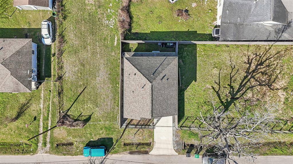 This aerial view shows a single-story home with a neatly maintained yard. The house has a driveway leading to the street, and it's flanked by green lawns and neighboring homes. The property appears spacious, with room for outdoor activities or potential landscaping.