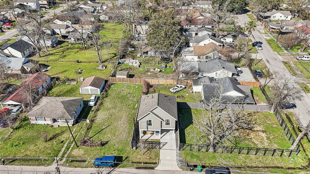 This aerial photo shows a residential neighborhood with a mix of single-family homes. The central property features a modern two-story house with a driveway, and a spacious, well-maintained yard. The area is characterized by greenery and mature trees, offering a suburban feel with nearby streets and neighboring homes.