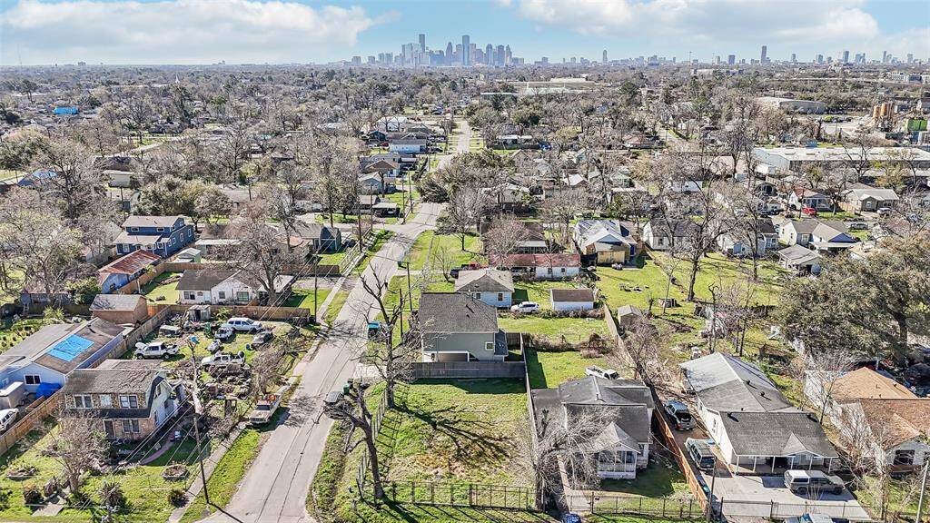 This aerial photo showcases a suburban neighborhood with tree-lined streets and a mix of charming homes. The area appears spacious and well-maintained, with a distant view of a city skyline, suggesting convenient urban access. Ideal for buyers seeking a balance of tranquility and city proximity.