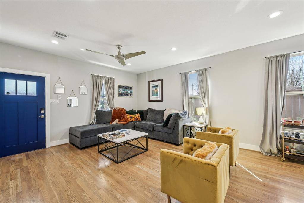 This open-concept living area features a modern kitchen with a central island, granite countertops, and stainless steel appliances. The space flows into a cozy living room with hardwood floors, neutral walls, and ample natural light from multiple windows.