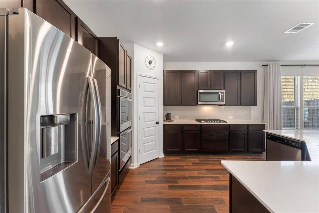 Energy Star stainless steel appliances elevate the space, including double ovens with a touch screen, a built-in microwave, a 30” 5-burner gas cooktop with griddle and Samsun double-door refrigerator that stays with the home.  Notice the upgraded five-panel door with sleek black iron hardware leading the corner walk-in pantry.