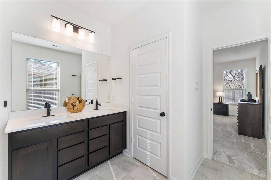The primary bathroom features tile flooring, an extended vanity with dual sinks, black matte Moen fixtures and Silestone countertops.