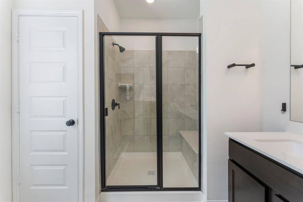 The primary bathroom has a large shower with tile surround, Bella seat, niche shelving and black matte Moen fixtures with glass enclosure.