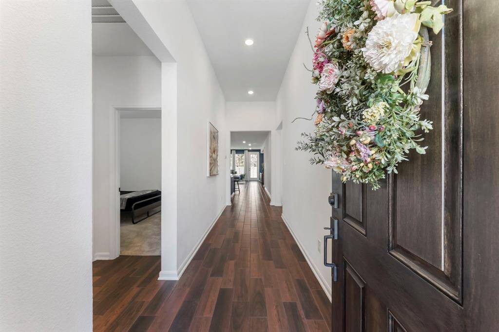 Step into this home through a long, welcoming hallway with beautiful wood-look tile flooring, complemented by soaring tall ceilings and an abundance of natural light.