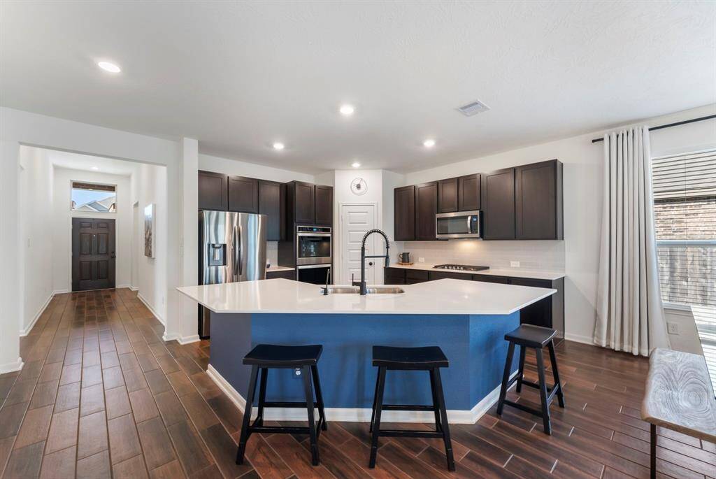 The well-designed kitchen has a large working island that offers additional seating, extra storage, a strategically placed Whirlpool AccuSense dishwasher and dual stainless-steel sink with a sleek black matte Moen faucet. A built-in charging port adds modern convenience.