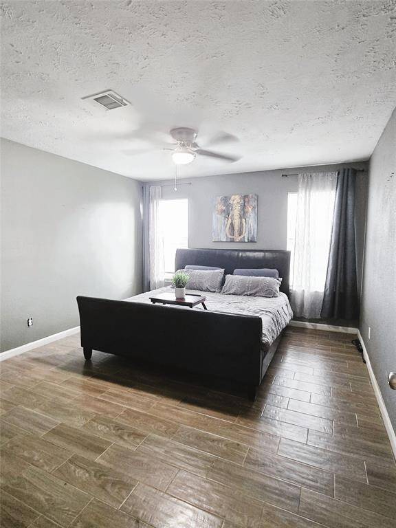 Primary Suite features wood-style flooring, ceiling fan, and two large windows allowing natural light.