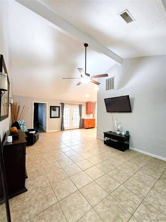 Spacious Family Room with vaulted ceiling, tiled flooring, ceiling fan and French doors leading to a covered patio.