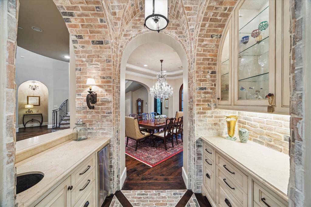 The wet bar area has exposed brick walls featuring arched doorways, drawers, display cabinets, ice maker creates a charming transition between the kitchen and the formal dining room.