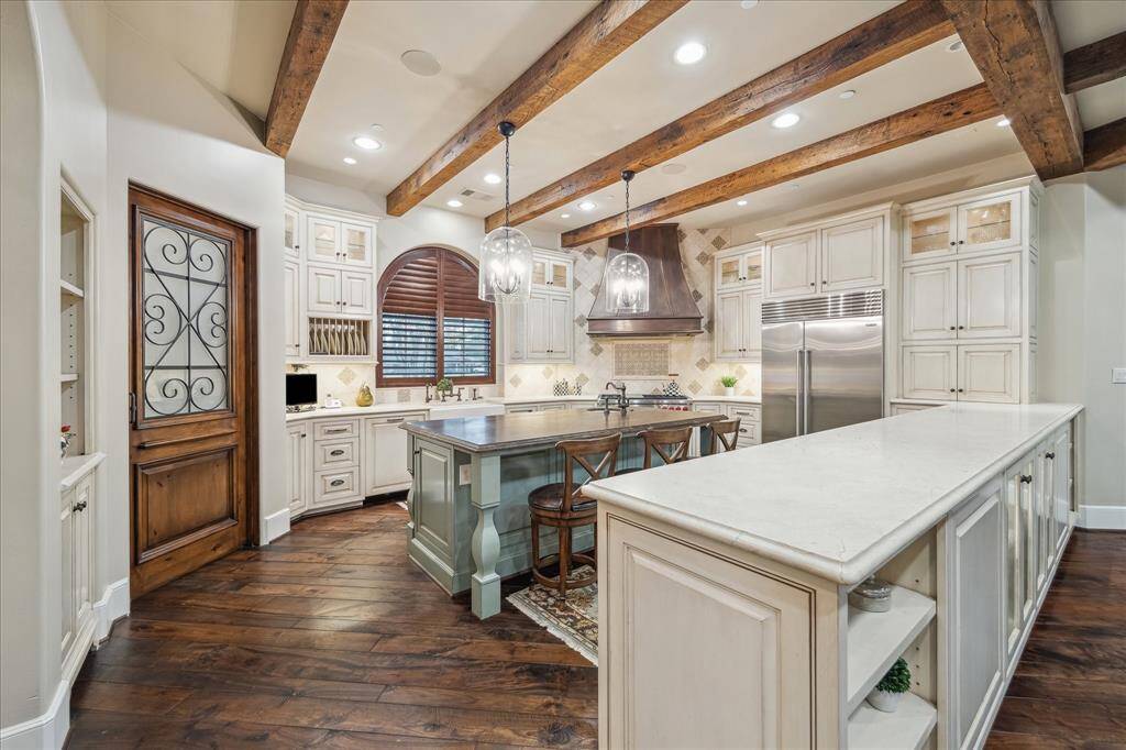 Kitchen features island with quartzite countertop and seating island, double sinks, a butler bar,  custom cabinets and a walk-in pantry with iron accented door.