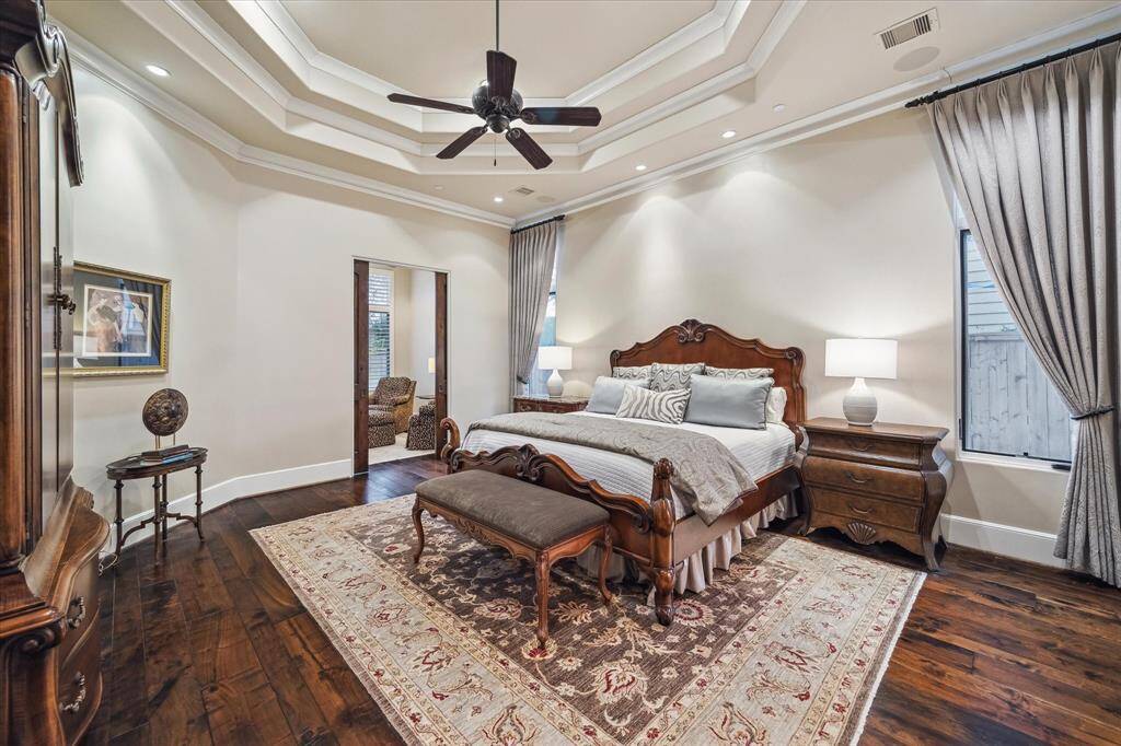 Primary bedroom features high ceilings with intricate tray detailing and crown molding and wood flooring.