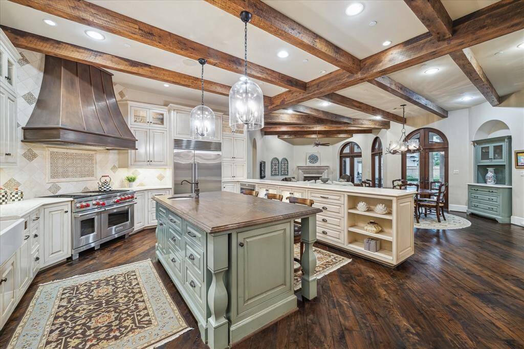 Kitchen with exposed wooden beams add a rustic and neutral element to the space. Luxury pendant lights above the island, provide ambient light and a touch of elegance.