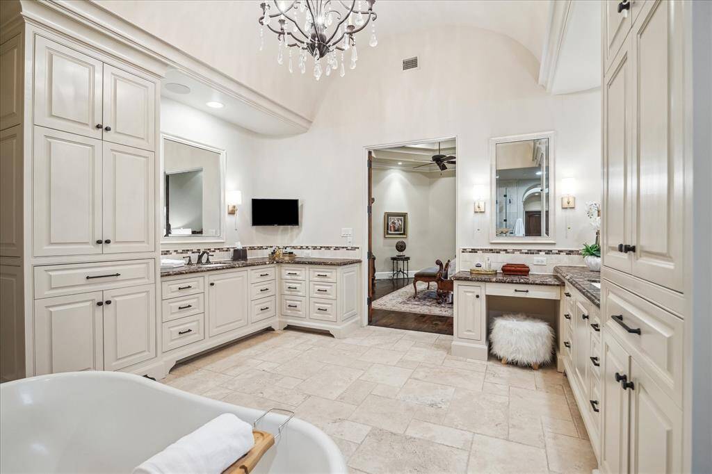 The en-suite bath features an arched alcove with a sparkling chandelier and mounted sconces. The extended double vanity, has abundant cabinets and drawers and water closet with bidet.