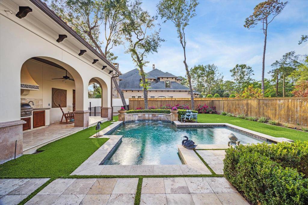 A picturesque backyard with sparkling pool, summer kitchen, outdoor full bath and natural grass.
