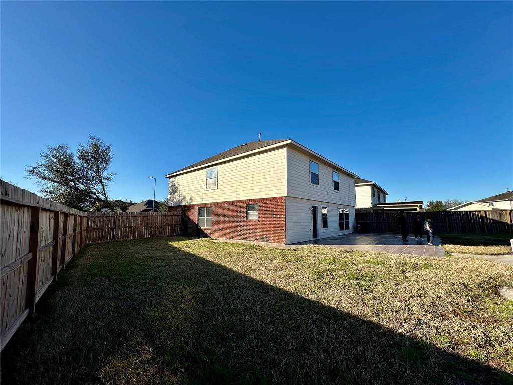 This photo shows a two-story house with a mix of brick and siding exterior. It features a spacious fenced backyard with a patio, ideal for outdoor activities. The area is grassy with ample space for landscaping or gardening.