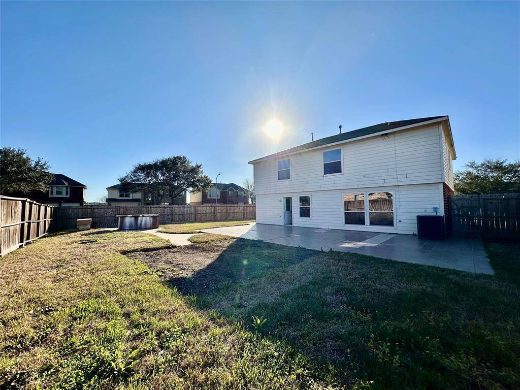 Spacious backyard with a large patio area, perfect for outdoor activities and entertaining. The two-story house features ample windows for natural light. The yard is fenced for privacy and security.