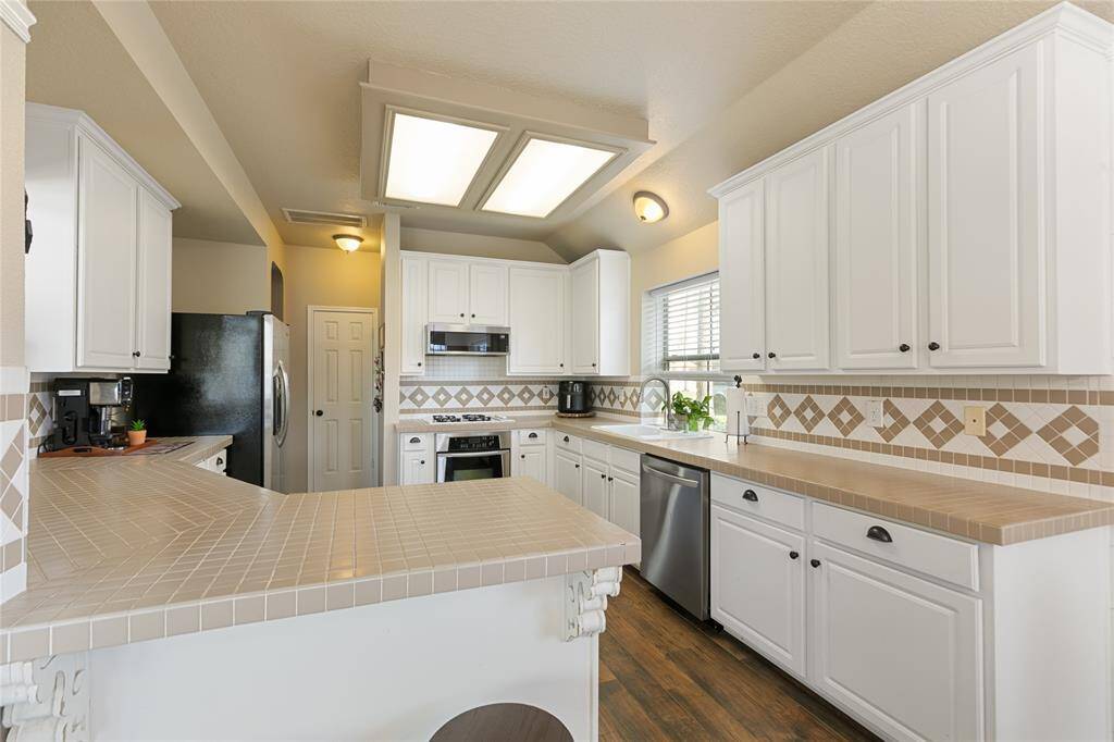 Kitchen features generous tile countertops with decritive backsplash, lots of cabinet space.