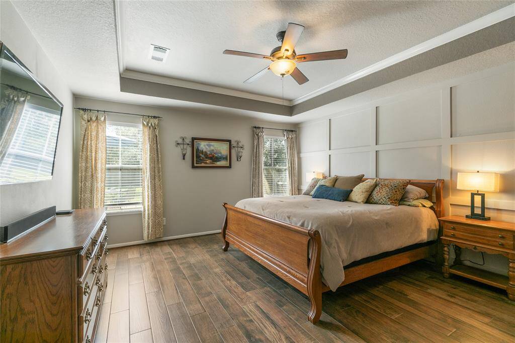Primary bedroom with tile woodlike floors, coffered ceiling w/molding and Grid patterned accent wall.