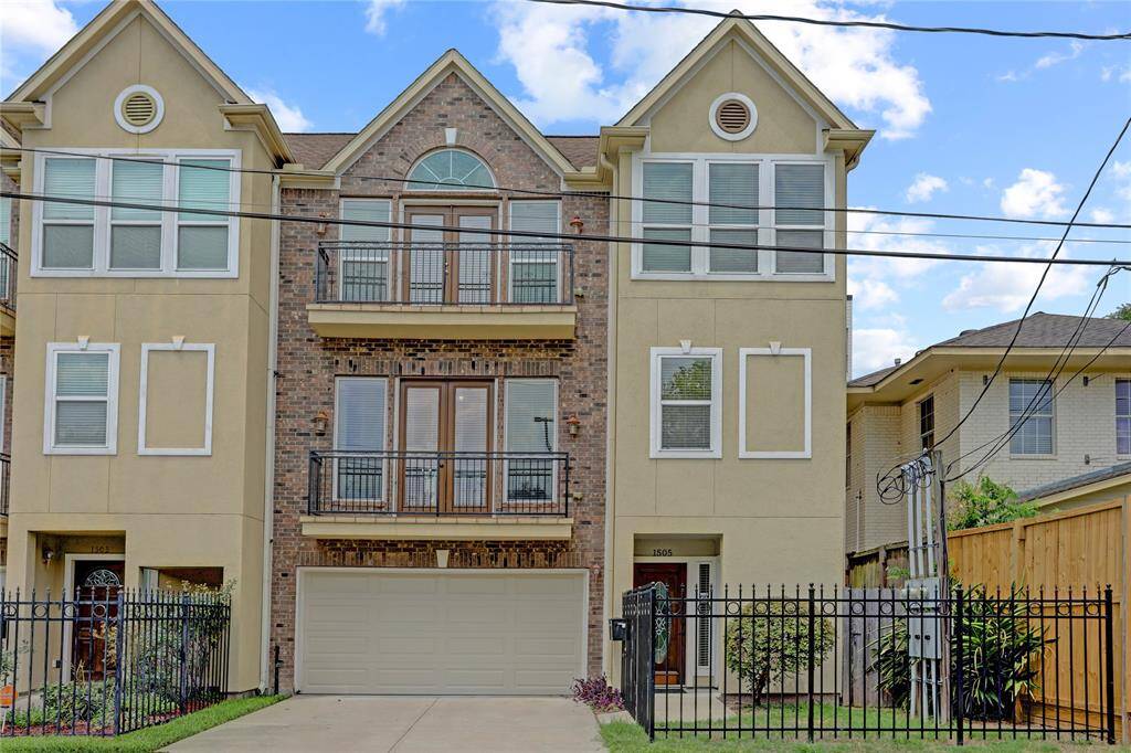 A beautifully designed three-story townhouse featuring a brick and stucco facade, a gated entrance, a private two-car garage, and a charming second-level balcony that enhances its curb appeal.