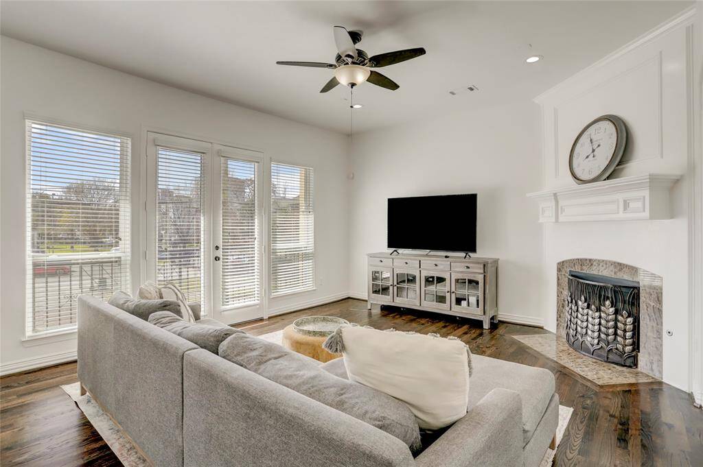 A sunlit living space boasting soaring ceilings, wood flooring, expansive windows, and an elegant fireplace as the focal point.