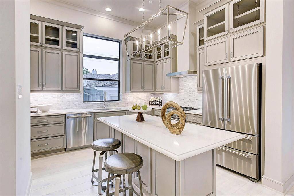This modern kitchen features sleek stainless steel Thermador appliances, ample cabinetry with a sophisticated gray finish, and a large island with seating. It offers a bright and airy atmosphere with high ceilings and stylish lighting, perfect for both cooking and entertaining. Refrigerator included.