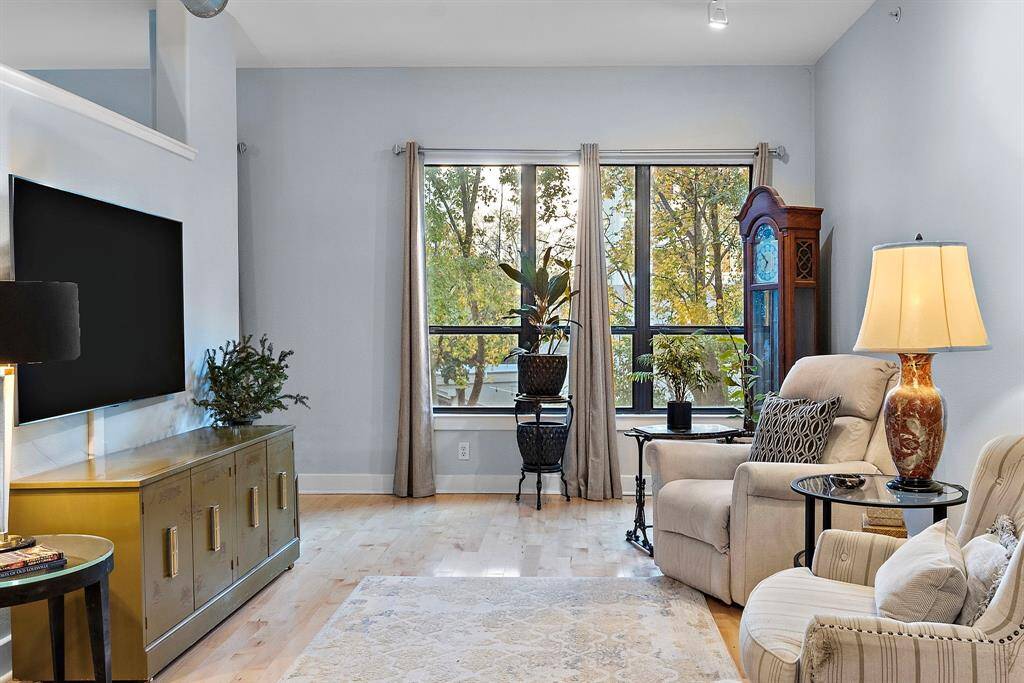 Elegant living area with plush seating in light, neutral tones, perfect for relaxation. Large windows frame lush outdoor views, while a sleek entertainment center adds sophistication to the room.