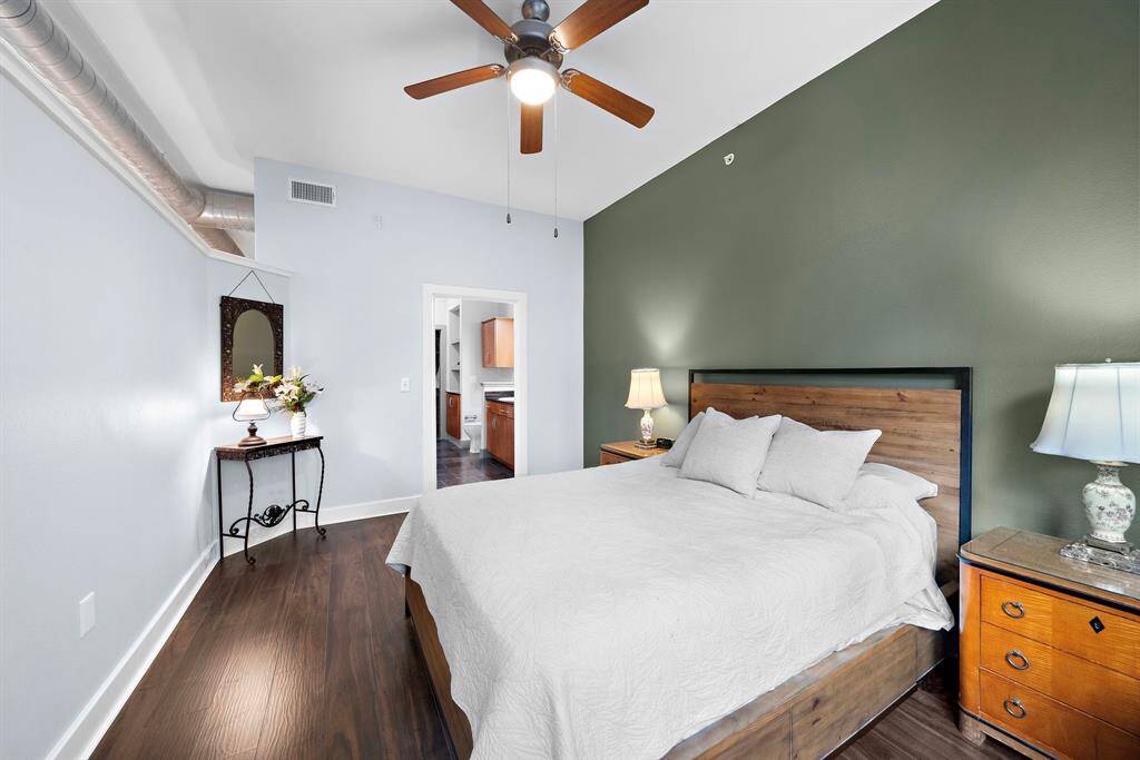The primary bedroom is a stylish sanctuary featuring dark wood flooring and an olive-toned accent wall giving a warm contrast to the light furnishings.