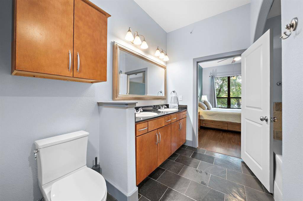 The bathroom offers a sleek retreat with double vanities, complemented by rich wood cabinetry and dark stone countertops.