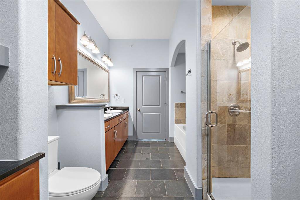 The modern bathroom boasts sleek slate tile flooring and natural stone shower surround, offering a spa-like retreat. Warm wood cabinetry and dual vanities provide ample storage and practicality, while contemporary light fixtures add a touch of elegance to this functional space.