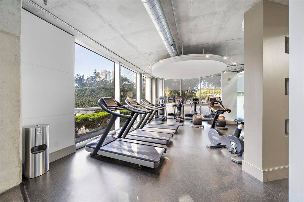A bright fitness center equipped with modern treadmills and elliptical machines, framed by floor-to-ceiling windows offering a lush outdoor view.