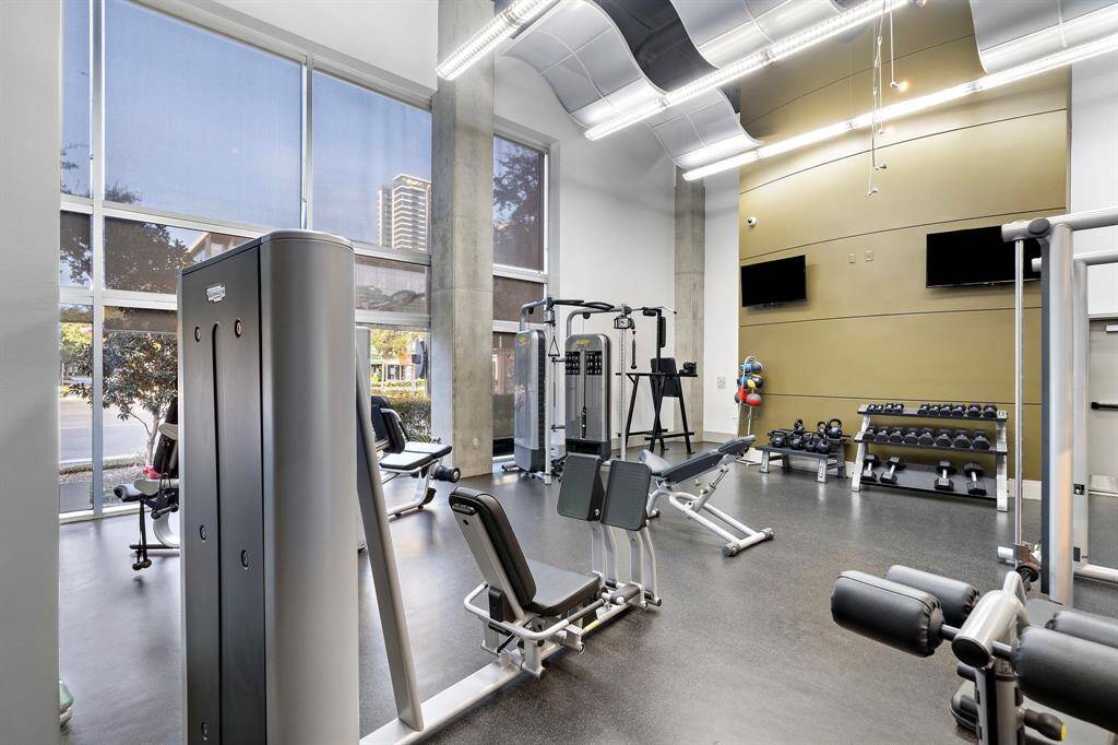 State-of-the-art fitness center featuring a variety of modern exercise equipment, including strength machines and free weights. The expansive windows provide abundant natural light and city views, enhancing your workout experience in a sleek, urban setting.