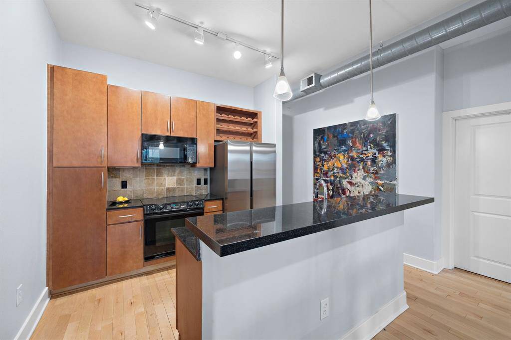 The kitchen showcases sleek modernity with stainless steel appliances and dark granite countertops, contrasting elegantly with warm wood cabinetry.