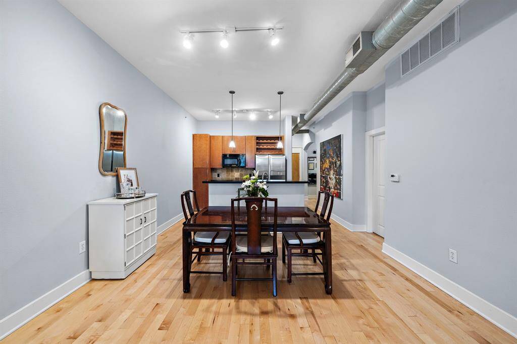 Experience dining elegance in this open-concept area featuring sleek wood flooring. The space flows seamlessly into a well-equipped kitchen with contemporary cabinetry and stainless steel appliances, perfect for hosting delightful meals and gatherings.