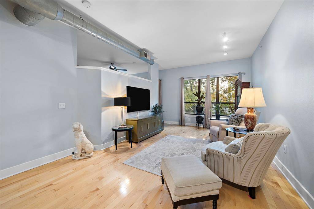 Discover the loft-style living room featuring exposed ductwork and warm natural wood floors. Large windows frame serene views, inviting ample natural light into this sophisticated space.