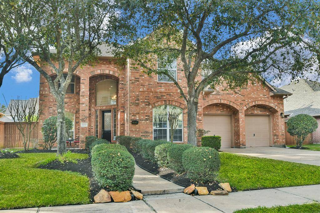Charming two-story brick home with a welcoming front walkway and lush landscaping. Features an attached two-car garage and large windows for natural light. The mature trees add to the curb appeal, creating a cozy, inviting atmosphere.