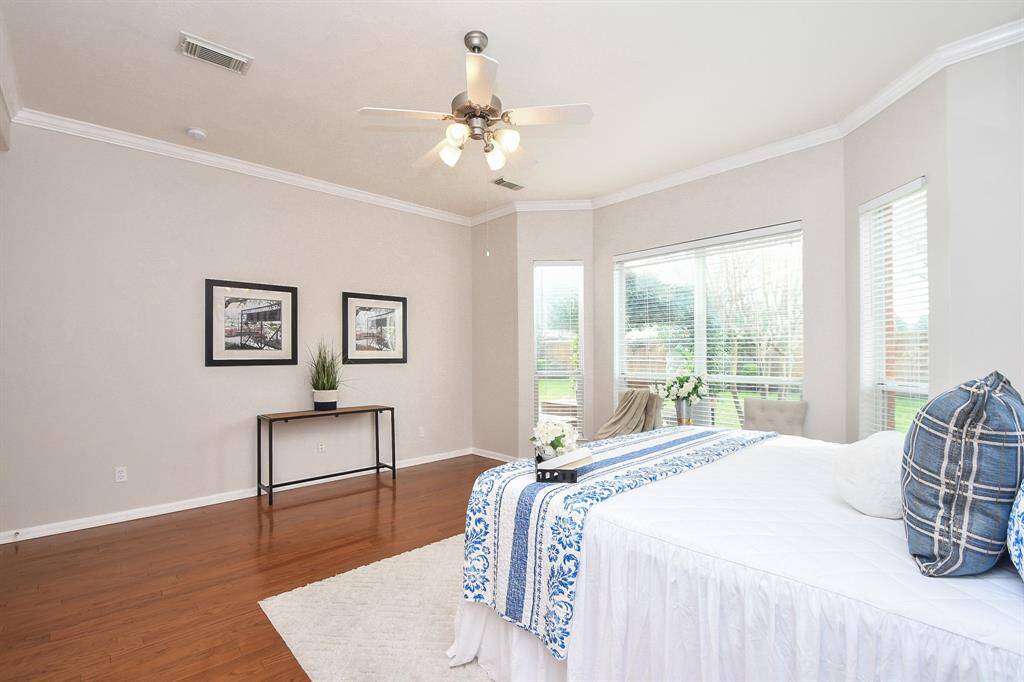 This freshly painted spacious bedroom features hardwood floors, large windows with garden views, and neutral walls. There is plenty of space for a dressing table and additional seating area.