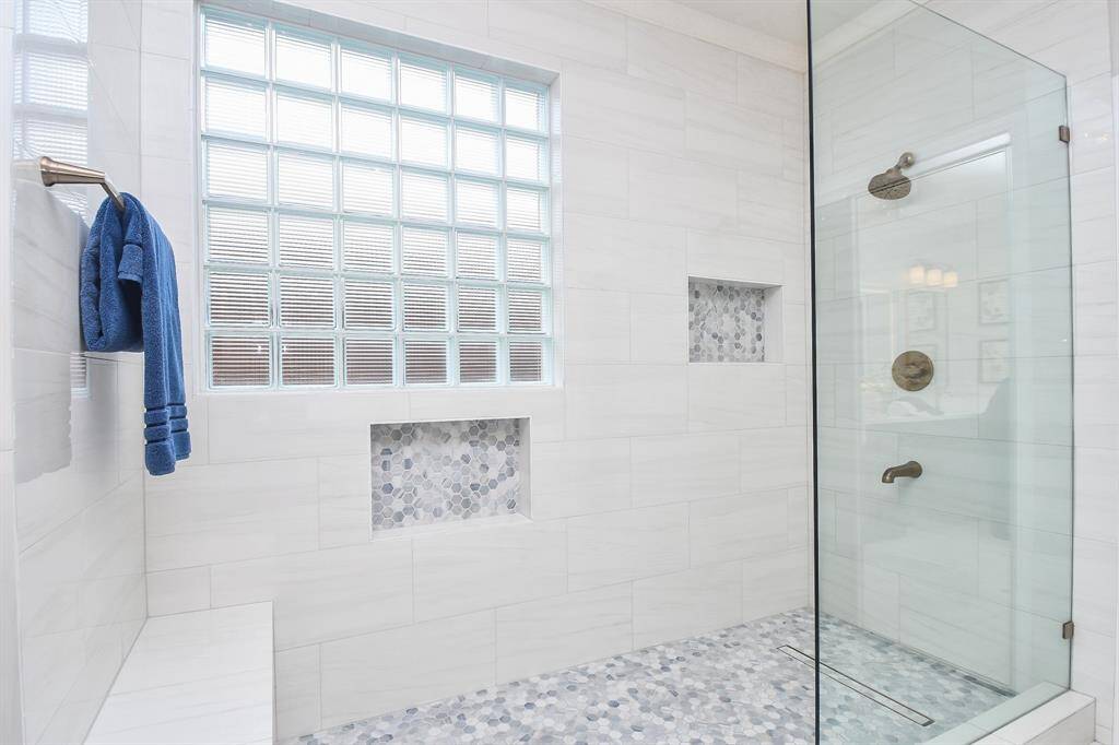 This photo showcases a modern bathroom with a spacious walk-in shower featuring glass doors, elegant tile work, and built-in niches. A window with glass blocks provides natural light, and a towel rack adds functionality.