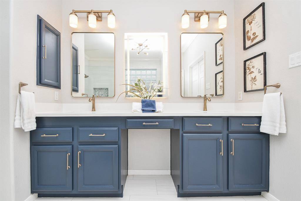 This bathroom features a stylish double vanity with elegant blue cabinetry, modern bronze fixtures, and ample lighting. The central LED (lighted) mirror provides extra light along with the two brand new fixtures with glass shades.